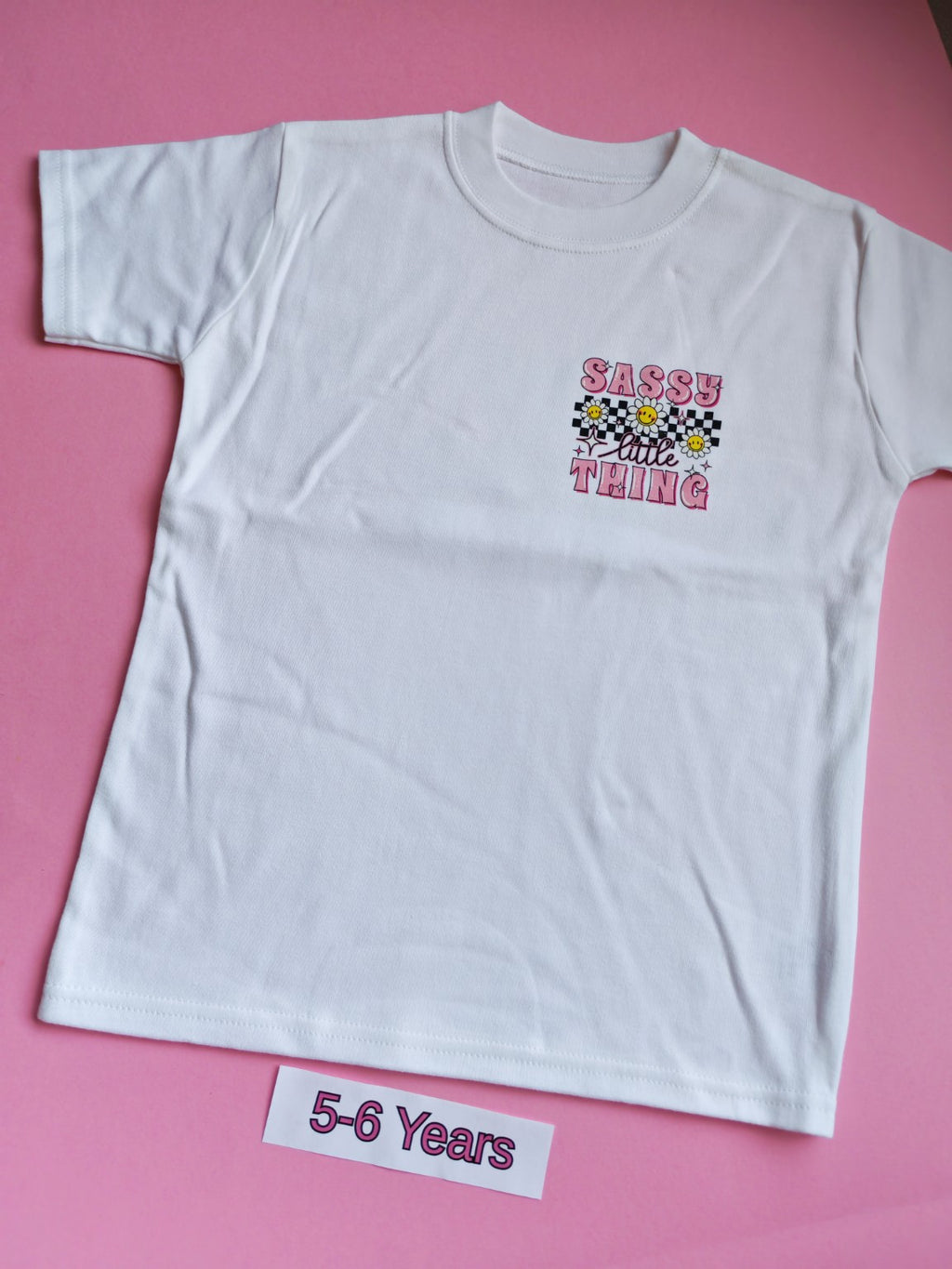 White children's t-shirt with pink Sassy Little Thing daisy and checkerboard design, 5-6 years, front